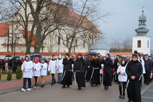Wierni wyruszajÄcy w DrogÄ KrzyĹźowÄ. Na pierwszym planie zakonnicy niosÄcy krzyĹź. W tle klasztor w Smardzewicach.