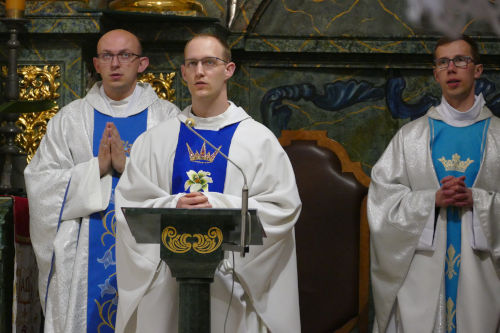 Trzech Neoprezbiterów modlących się przy Ołtarzu w ornatach z błękitnymi akcentami.