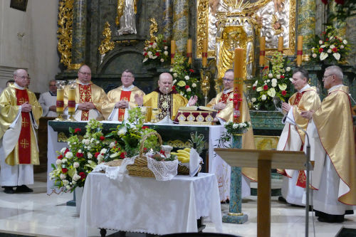 Siedmiu kapłanów odprawiających Mszę Świętą przy ołtarzu. Przed ołtarzem ustawione są przyniesione dary.