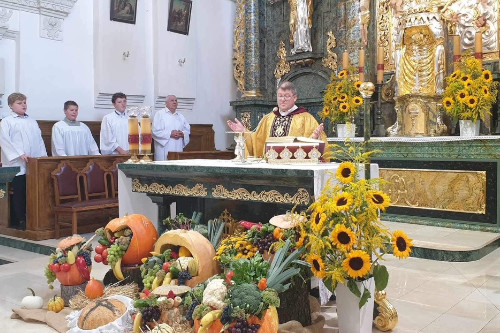 Ojciec Mariusz Kapczyski modlcy si przy Otarzu przyozdobionym sonecznikami oraz darami, takimi jak dynie, chleb.