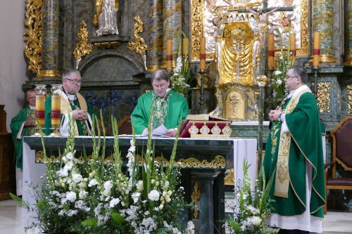 Trzech Księży stojących przy Ołtarzu w zielonych ornatach.