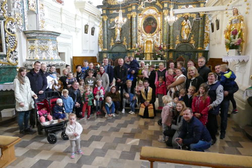 Rodziny stojące przed Ołtarzem w półokręgu. Pośrodku klęczy Ksiądz.