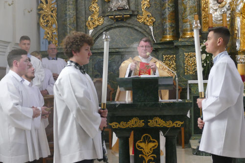 Ksiądz Proboszcz kadzący ambonę. Przed amboną stoi dwóch ministrantów ze świecami. Po lewej stronie stoją kolejni ministranci.